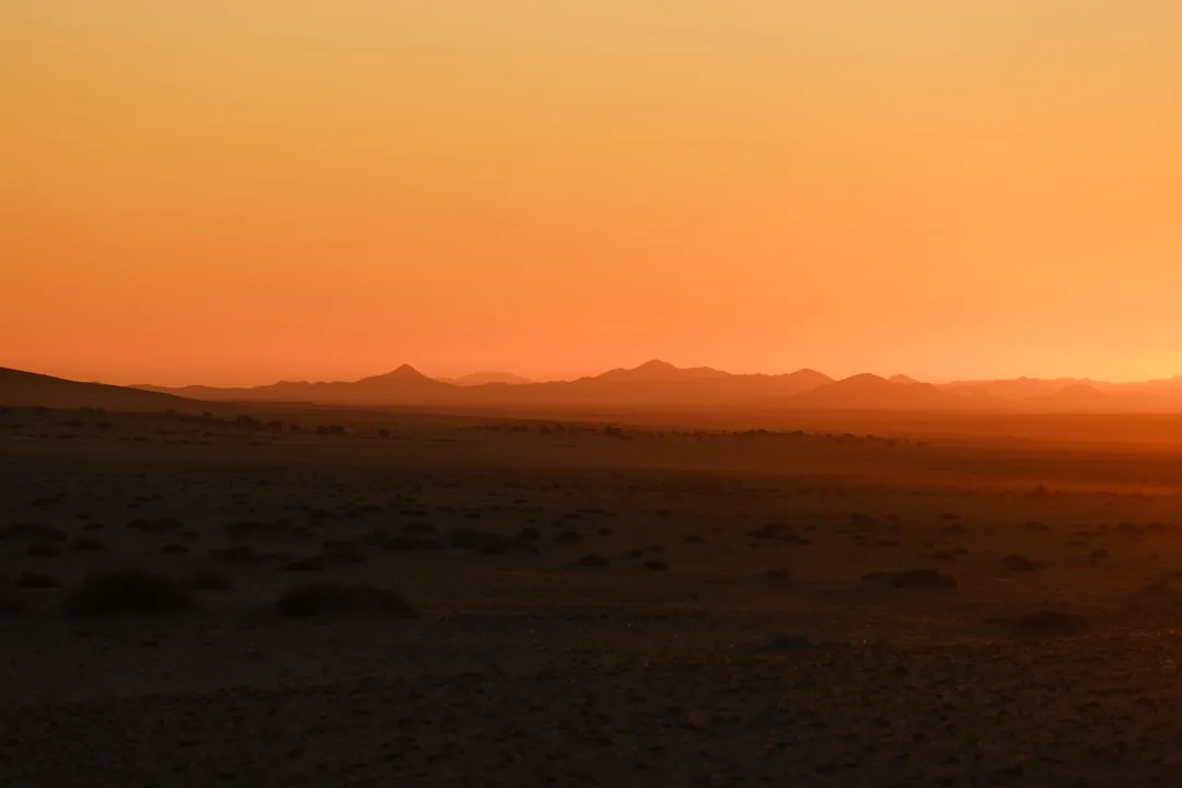 The sun is setting in the desert with mountains in the background
