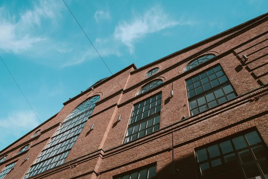 Low angle shot of a historic brick building with glass windows against a blue sky.