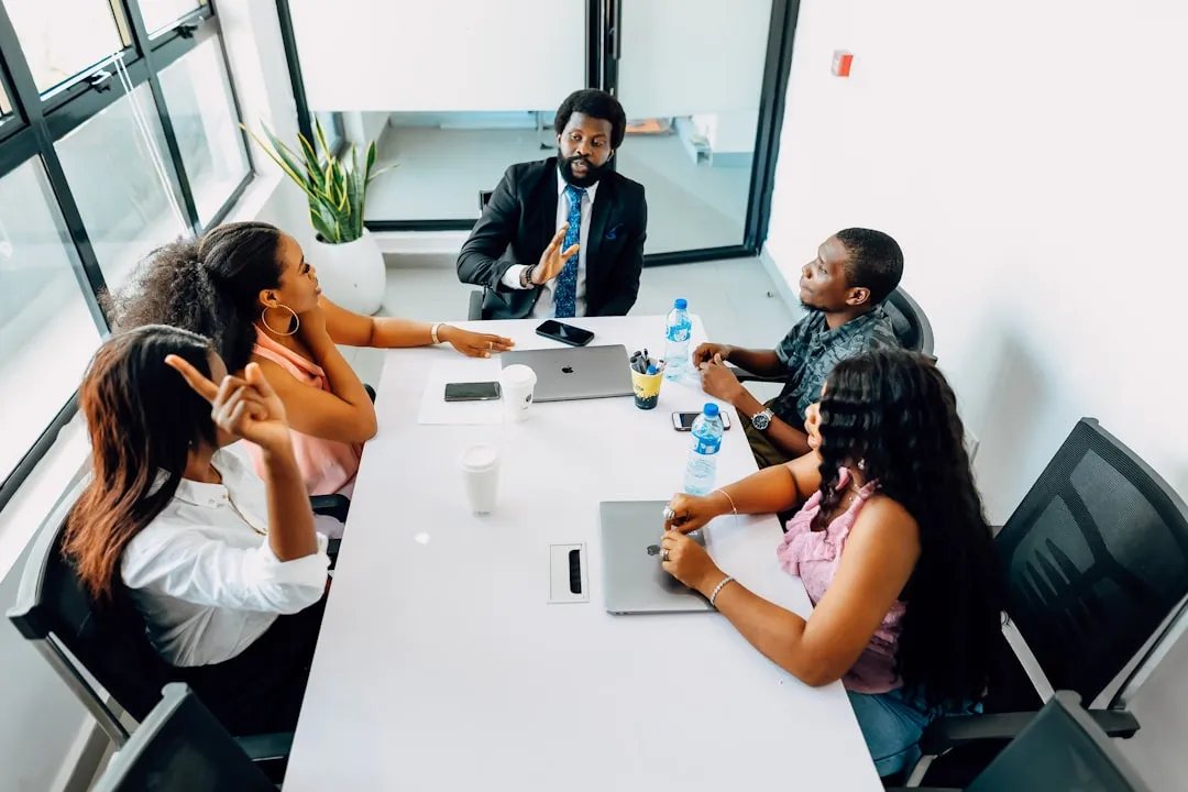 A group of people sitting around a white table in a meeting